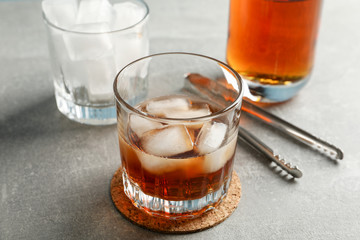 Bottle, glasses with ice cubes and whiskey on grey background, close up