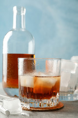 Bottle, glasses with ice cubes and whiskey on grey background, close up