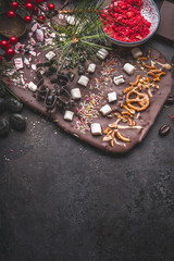 Obraz na płótnie Canvas Chocolate bark with topping of caramel, marshmallows, nuts and candy . Christmas sweet gifts preparation on dark background with copy space. Top view