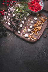 Chocolate bark with topping of caramel, marshmallows, nuts and candy . Christmas sweet gifts preparation on dark background with copy space. Top view