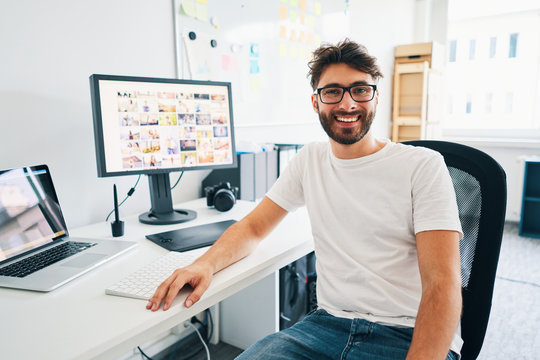 Portrait of happy photographer sitting by desk with computer at his studio