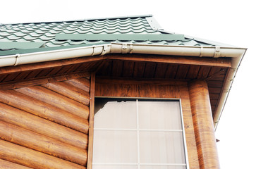 Roof made of metal with a gutter and a drainpipe. Log house with a roof made of iron tiles and a rain gutter, close up side view.