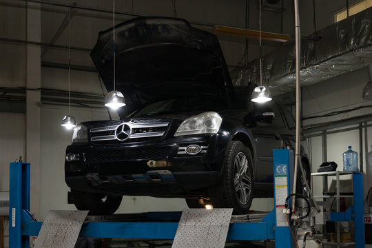 Used black car Mercedes Benz GL with an open hood raised on a four-post lift for repairing the chassis and engine in a vehicle repair shop. Auto service industry.