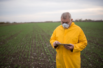 Farmer in yellow coat, controls the work in the field over its tablet.