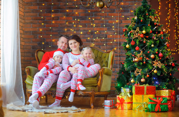 Portrait of a happy family sitting in pajamas in a chair near the festive Christmas tree and...