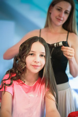 Fototapeta premium Beautiful woman curls long hair to the girl using curling iron