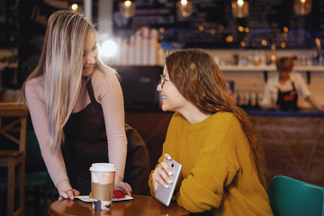 Young pretty woman and waitress in cafe.