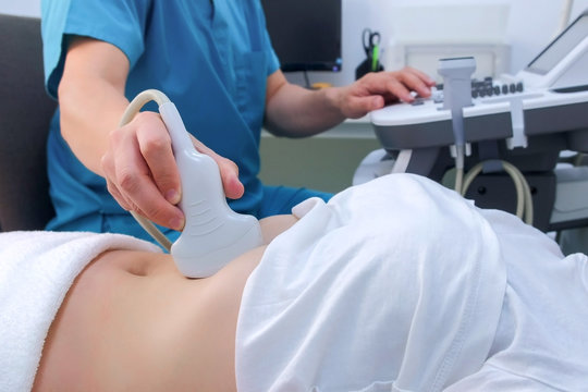 Ultrasound diagnostic of stomach on abdominal to woman in clinic, closeup view. Doctor runs ultrasound sensor over patient's girl tummy and looks at image on screen. Diagnosis of internal organs.