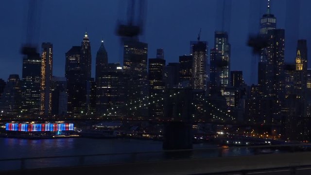 Dynamic shot of the Brooklyn Bridge at night with Manhattan skyscrapers skyline in the background, taken while crossing the Manhattan Bridge