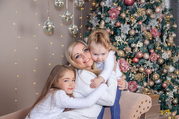 Mom and daughters at the Christmas tree. Christmas season. Sisters. Merry Christmas and happy holidays Cheerful mom and her cute daughters exchange gifts.