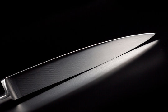 Kitchen knife with a white handle on a black background. A sharp blade of a knife.