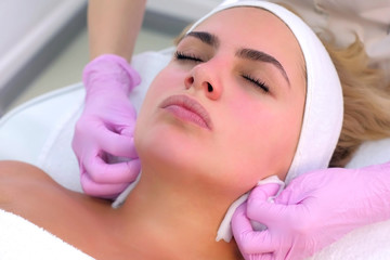 Portrait of woman client on facial cleansing procedure that washes hands of beautician. Cosmetologist making beauty procedure to patient relaxing in clinic. Beauty industry concept.