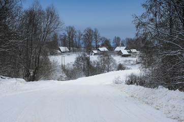 Winter landscape with road leading to village houses with snow covered roofs and smoke over chimneys