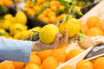 Woman hand choosing lemons at supermarket. Concept of healthy food, bio, vegetarian, diet.