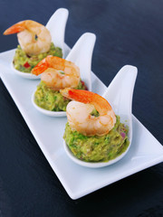 Canapes with avocado spread and shrimp served on white porcelain appetizer tasting spoon over black slate tray.