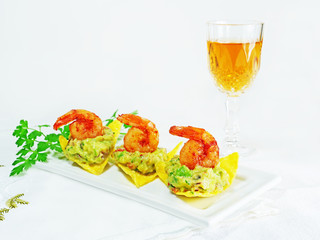 Canapes with guacamole and shrimp served on crispy tortilla chips on white serving plate