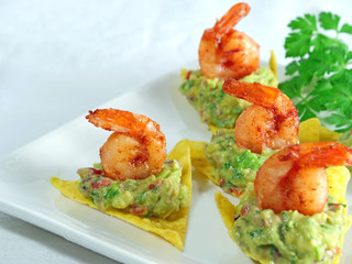 Canapes with guacamole and shrimp served on crispy tortilla chips on white serving plate