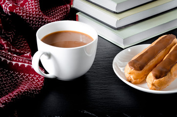 A round white cup and saucer stands on a white wooden table next to books and yellow autumn leaves