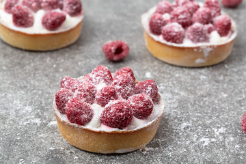 Delicious raspberry tart (tartlet) with whipped cream and raspberries on gray background. Delicious dessert.