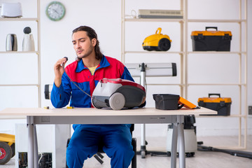 Young male contractor repairing vacuum cleaner at workshop