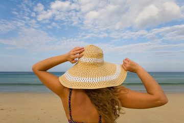 Rear view of a natural blonde in a hat that looks at the sea horizon.