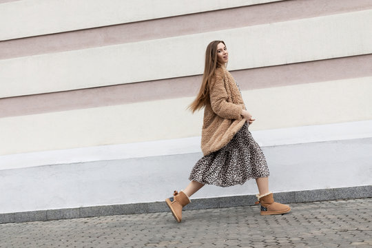 artificial fur coat, long leopard print dress, ugg boots, a small shoulder bag, a beautiful white model girl with long hair poses cheerfully walks on the street near the wall