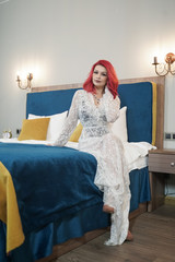 beautiful bride girl with red bob haircut in lace long dress posing in her bedroom alone