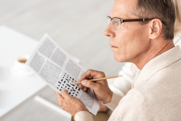 Fototapeta na wymiar selective focus of senior man in glasses holding pencil near crossword in newspaper