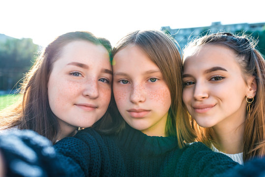 Girls teenage schoolgirls take pictures on a phone, selfie picture, happy smiling, emotions of joy, delight and fun, warm sweaters in autumn on street in city. Best friends girlfriends.