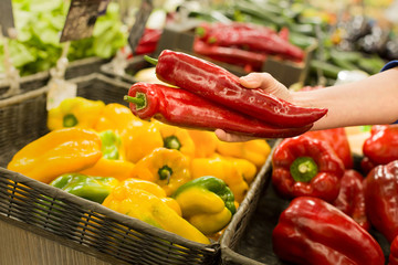 Female hand choosing fresh pepper in supermarket. Concept of healthy food, bio, vegetarian, diet.