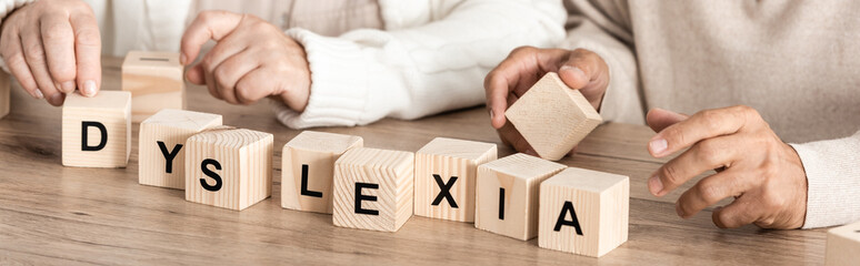 panoramic shot of senior woman sitting near sick husband and wooden cubes with dyslexia letters