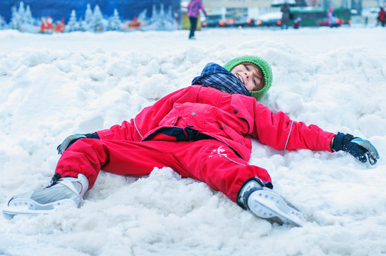 A tired child lies in the snow near the skating rink with his legs spread on the sides. Winter outdoor activities and outdoor sports. Fatigue from ice skating. Have fun until you drop