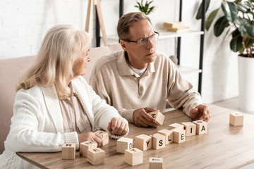 senior woman looking at sick husband near wooden cubes with dyslexia letters