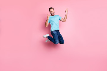 Turned full length body size photo of crazy insane man showing double rock horned fingers sign screaming in jeans denim jumping isolated pastel color background