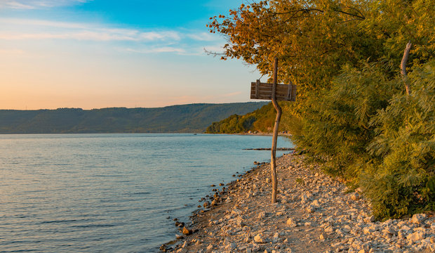 calm picturesque silent lake forest edge shore line scenery landscape photography with wooden pointer near trees in soft colors evening peaceful time before sunset, empty copy space for text 