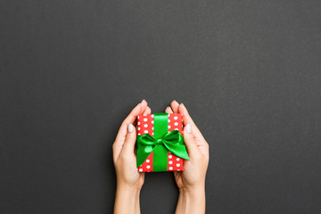 Top view of female hands holding christmas or other holiday handmade present box package in the palms, flat lay on black background with copy space
