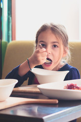 Beautiful child eats soup from a white plate in a cafe