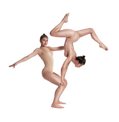 Fototapeta na wymiar Two flexible girls gymnasts in beige leotards are performing exercises using support and posing isolated on white background. Close-up.