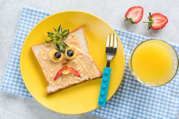 Peanut Butter Sandwich With Funny Angry Face And Glass Of Orange Juice For Kids. Table Top View. Healthy Food