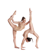 Obraz na płótnie Canvas Two flexible girls gymnasts in beige leotards performing complex elements of gymnastics using support, posing isolated on white background. Close-up.
