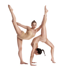 Two flexible girls gymnasts in beige leotards performing complex elements of gymnastics using...