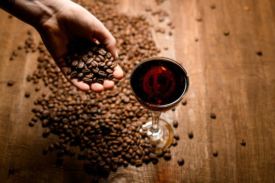 Alcoholic brown cocktail in the glass standing on the wooden table with coffee beans sprinking by bartender