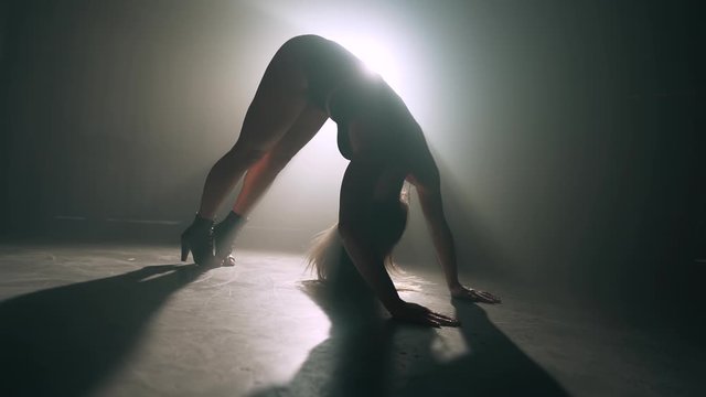 Female silhouette in bright spotlight.Professional dancer moves on stage to music.Plastic girl with sporty and seductive figure.