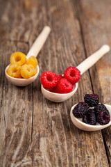 Ripe red and yellow raspberries and blackberries in spoons