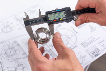 Hands of an engineer measures a metal part with a digital vernier caliper against the background of...