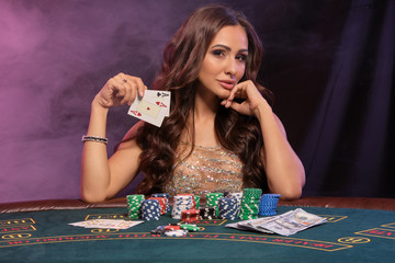 Girl playing poker, casino. Showing cards, sitting at table with stacks of chips and money. Black,...