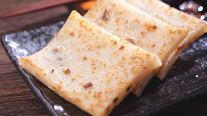 Pouring black soy sauce on ready-to-eat delicious turnip cake, Chinese traditional local dish radish cake in restaurant, close up, copy space.