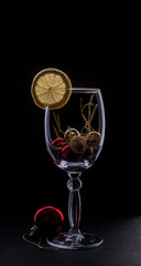 Bright silhouette of a glass with a slice of lemon and red christmas and new year ball isolated on a dark background. Dark mode