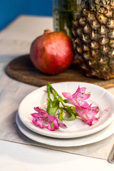 Tropical paradise heaven asian  pink iris flower on white plate, pineapple, pomegranate  in spa resort, restaurant. Holidays rest at sea. Food of gods. Table setting decoration with fork knife