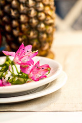 Tropical paradise heaven asian thai pink iris flower on white plate, pineapple, pomegranate on wooden tray in spa resort, restaurant. Holidays rest at sea. Food of gods. Table setting decoration